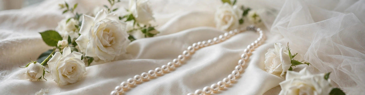 White freshwater pearl necklace draped across ivory bridal silk with white roses and a sheer veil in soft window light