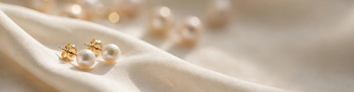 Freshwater pearl stud earrings resting on ivory silk fabric with soft warm light